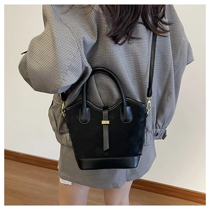 Détail du sac seau noir contrasté avec boucle dorée porté à l'épaule par un mannequin