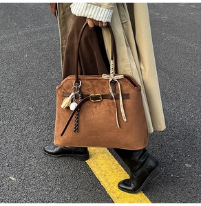 Detail view of large brown suede tote bag with decorative charms on a street background