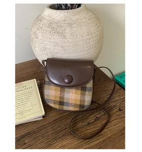 Detailed close-up of a retro plaid saddle bag with dark brown leather flap and round buckle