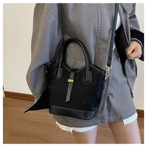 Détail d'un sac seau noir mat avec boucle dorée et bandoulière réglable sur l'épaule