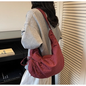 Detail view of red checkered canvas dumpling bag with side drawstring worn on shoulder