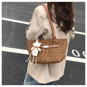 Outdoor street view of a leopard print suede tote bag with a cute bear pendant charm