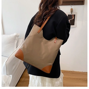 Detail of khaki tote bag with brown leather corners held by a model in casual attire