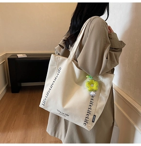 Detail of cream canvas tote bag with black lettering and yellow flower plush charm
