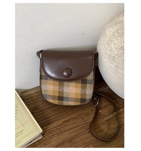 Detailed close-up of a vintage saddle bag in brown leather and plaid fabric on a wooden table