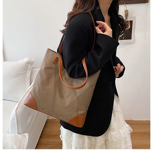 Detail of khaki nylon tote bag with leather straps worn by model in a minimalist studio