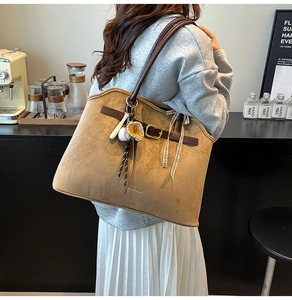 Detail of camel suede tote bag with metal buckle, ribbon, and baseball charms