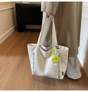 Detail of canvas tote bag with Lifelife text and a yellow daisy flower keychain charm