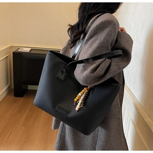 Détail du sac cabas noir avec pendentif perlé sur un manteau en laine chevron