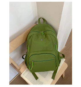 Detail eines grünen Nylon-Rucksacks mit Reißverschlusstaschen und Logo auf einem Holzstuhl