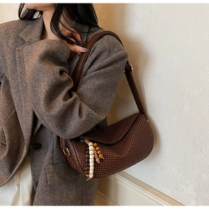 Detail of a brown woven dumpling bag featuring a beaded tassel and leather shoulder strap