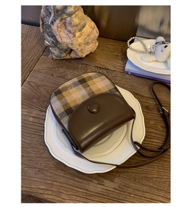 Detail view of a vintage saddle bag featuring brown leather and checkered fabric texture