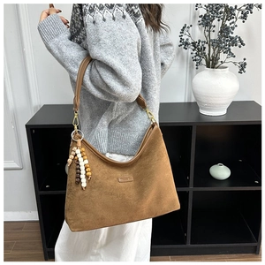 Detail view of brown suede underarm bag featuring colorful beaded tassel and gold hardware