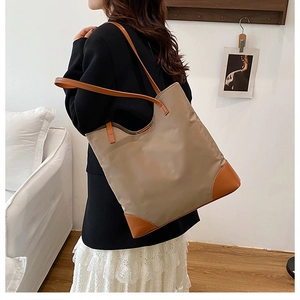 Detail of khaki tote bag with orange leather handles shown on shoulder with minimalist decor