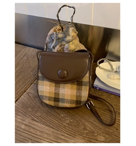 Detail view of vintage brown leather and plaid fabric saddle bag with adjustable strap