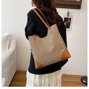Detail of khaki nylon tote bag with brown leather straps worn on shoulder by model
