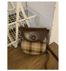 Detail of vintage saddle bag featuring retro clasp and brown plaid wool fabric texture