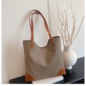 Detail of a khaki nylon tote bag with leather reinforced corners on a white book