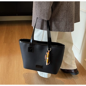 Vue de dessus d'un grand sac cabas noir avec pompon en perles et écusson logo en cuir