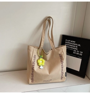 Detailed view of beige canvas tote bag with Life lettering and yellow flower charm decoration