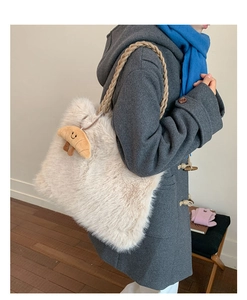 Detail view of cream plush faux fur tote bag with a croissant charm and woven shoulder strap