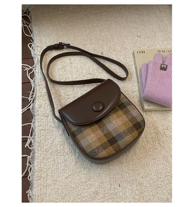 Close-up of a plaid stitching saddle bag in dark brown leather on a soft rug