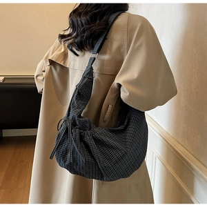 Detail shot of a plaid canvas hobo bag worn with a beige trench coat for casual styling