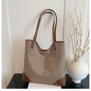 Detail of khaki tote bag with brown leather handles and reinforced base on a display box