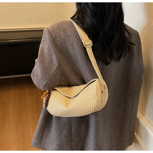 Detailed macro view of beige woven straw shoulder bag with adjustable leather strap and beads