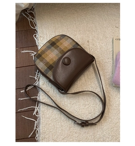 Detail of vintage saddle bag with brown leather and retro plaid fabric on plush carpet