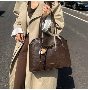 Detail of dark brown faux suede tote bag featuring a metal lock strap and stylish charms