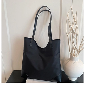 Detailed close-up of large black tote bag with reinforced leather corners and leather straps