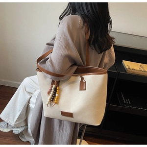 Détail d'un sac cabas en toile avec bordure en cuir marron et pendentif perlé coloré