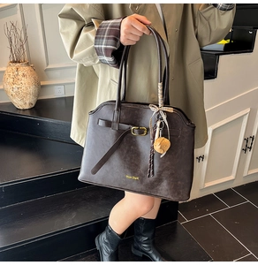 Detail of deep brown suede tote bag with gold buckle, silk scarf, and brand logo charm