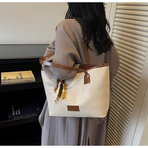 Détail d'un grand sac fourre-tout en daim beige avec bordure en cuir marron et bijou de sac