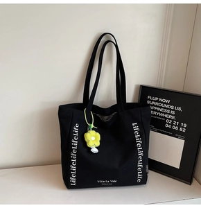 Close-up of black canvas tote bag with white art text and yellow sunflower charm