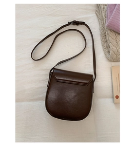 Detail of dark coffee matte leather saddle bag with silver buckle on a white cloth surface
