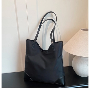 Close-up of black nylon tote bag with leather corner accents in a minimalist indoor setting