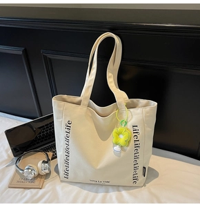 Detail of off-white canvas tote bag with black typography and yellow sunflower pendant
