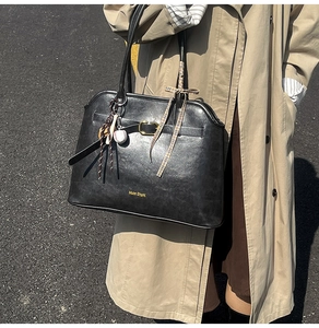 Detail of black faux leather tote with golden Muon SharK logo and baseball charm accessory