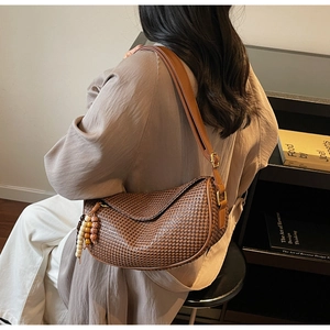 Close-up of brown woven dumpling bag with leather strap and decorative beaded tassel charm