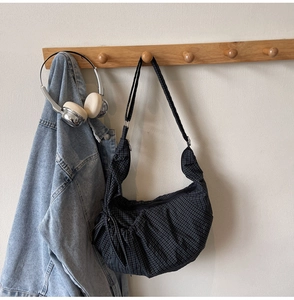 Detail of checkered canvas crescent shoulder bag hanging on a wooden hook in a room