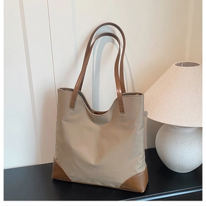Minimalist khaki tote bag with brown leather handles placed on a dark sleek tabletop