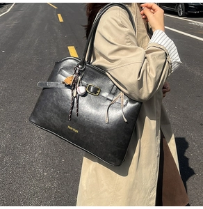 Detail of black faux leather tote bag with gold buckle strap and stylish baseball charms