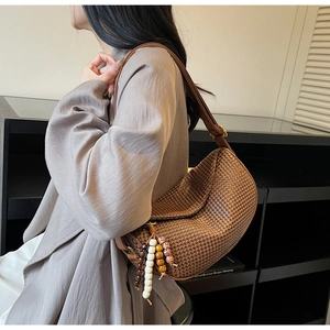Detailed view of woven straw dumpling bag featuring colorful bead charms and leather strap