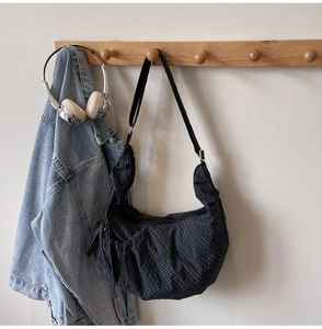 Close-up of black and white checkered crescent bag with adjustable strap on wooden hook