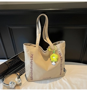 Detail of canvas tote bag with Life lettering and yellow flower charm on a desk