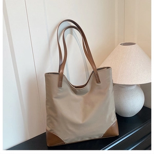 Detail of khaki nylon tote bag with brown leather handles on a minimalist desk