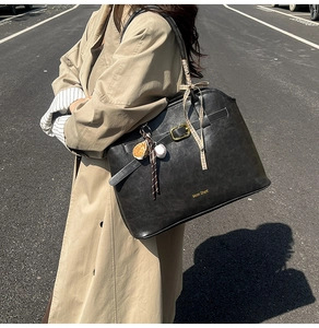 Detail of large black faux suede tote bag with ribbon and baseball charm on a model