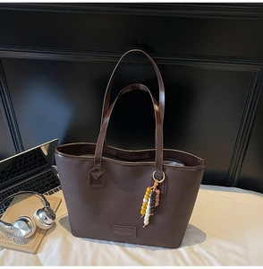 Gros plan d'un sac cabas en cuir marron avec breloque rétro sur un lit blanc doux
